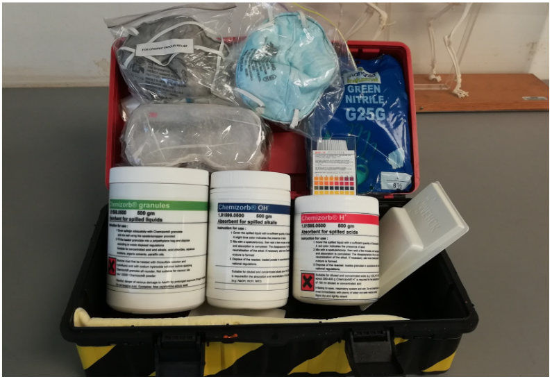 Open chemical spill kit showing absorbents for acids, alkalis and liquids, goggles, mask, gloves and pH strips